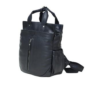 Puede incluir: Una mochila de color azul marino oscuro con acabado liso, que cuenta con dos asas superiores, un bolsillo frontal vertical con cremallera y bolsillos laterales con aberturas elásticas. Incluye correas ajustables y detalles metálicos.