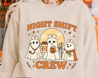 May include: Sand-colored sweatshirt with a Halloween-themed graphic. The design features three ghost characters dressed as nurses, the words "NIGHT SHIFT CREW", and medical-related icons. A fast shipping truck graphic is also present.