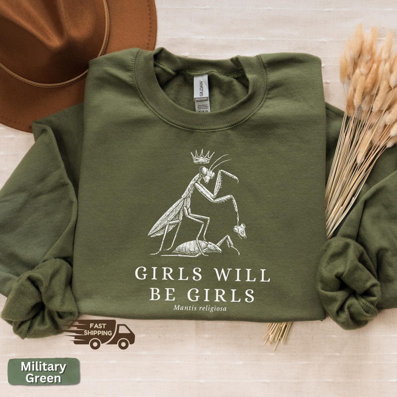 May include: Military green sweatshirt with a white graphic of a praying mantis wearing a crown, holding a smaller insect. Text reads "GIRLS WILL BE GIRLS" and "Mantis religiosa".