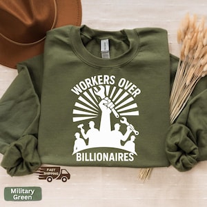 May include: Military green sweatshirt with the text "WORKERS OVER BILLIONAIRES" in white. The graphic features a raised fist holding a wrench, with silhouettes of workers and tools. The sweatshirt is a Gildan brand.