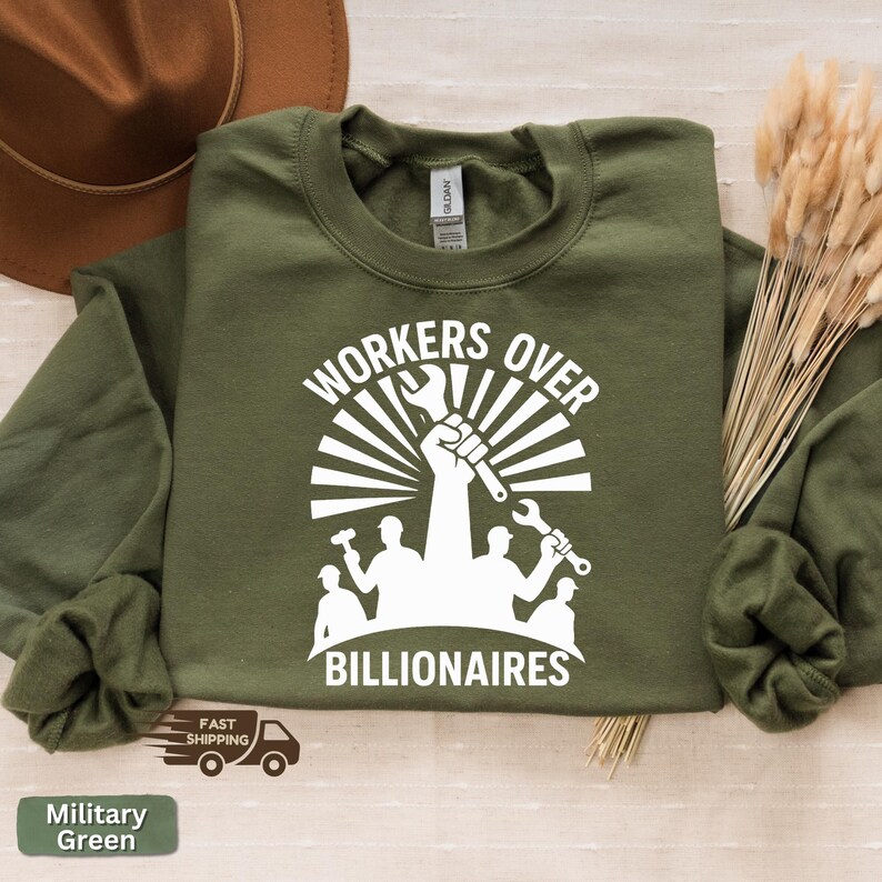 May include: Military green sweatshirt with the text "WORKERS OVER BILLIONAIRES" in white. The graphic features a raised fist holding a wrench, with silhouettes of workers and tools. The sweatshirt is a Gildan brand.