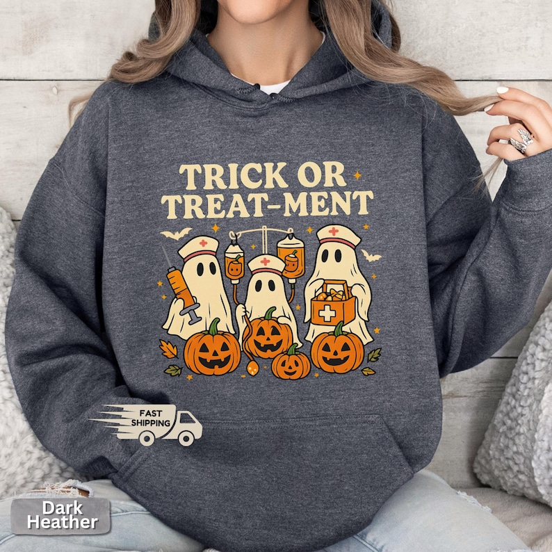 May include: Dark heather gray hoodie with a Halloween-themed graphic. The design features ghosts wearing nurse hats, pumpkins, and the text "TRICK OR TREAT-MENT". The graphic is in shades of orange, white, and beige.