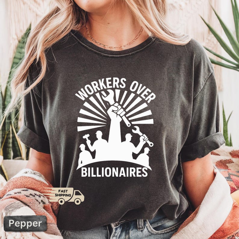 May include: Dark gray t-shirt with a white graphic. The graphic features the text "WORKERS OVER BILLIONAIRES" above a raised fist holding a wrench, with silhouettes of workers below. The shirt has rolled-up sleeves.