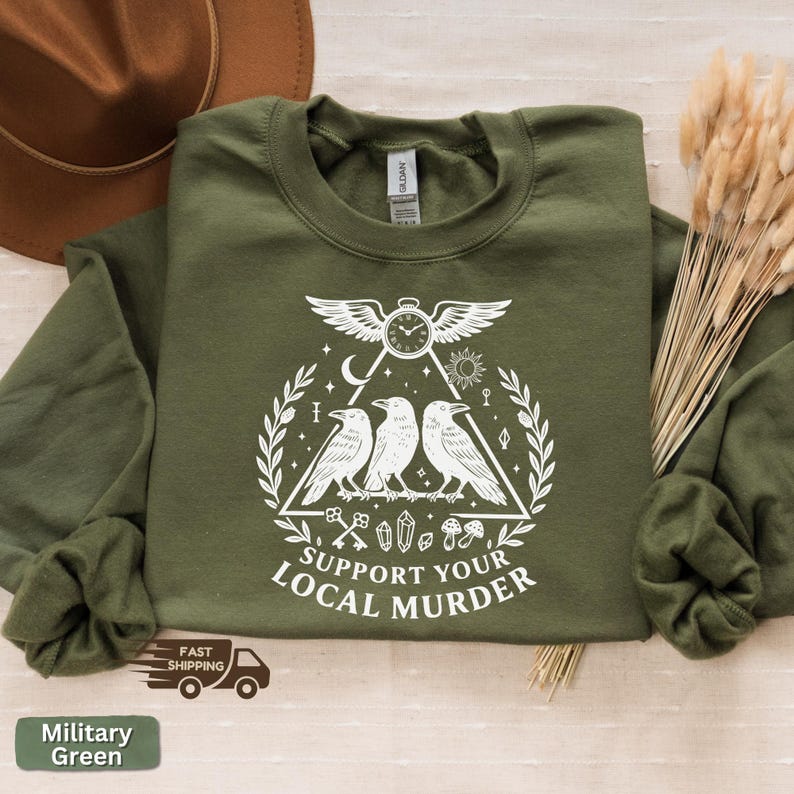 May include: Military green sweatshirt with a white graphic featuring three crows, a clock, and the text "SUPPORT YOUR LOCAL MURDER." The sweatshirt is made of a soft material and has a crew neck.