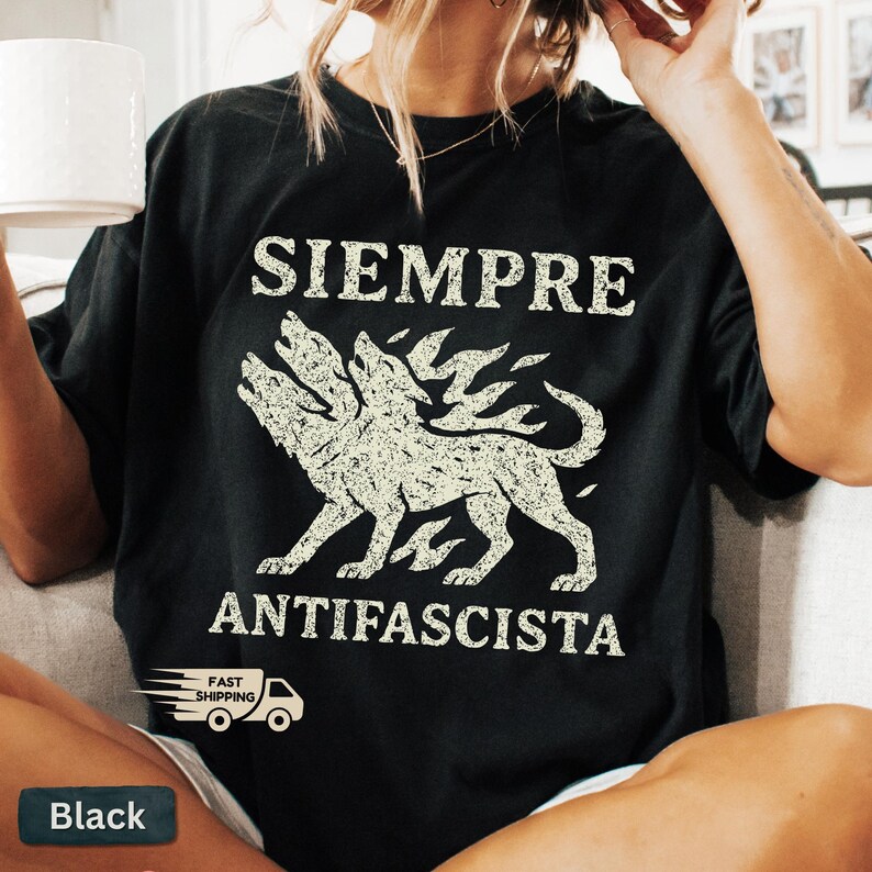 May include: Black t-shirt with the words "SIEMPRE ANTIFASCISTA" in white, along with a three-headed dog graphic. The shirt has a vintage, distressed look. A small "Fast Shipping" logo is visible.