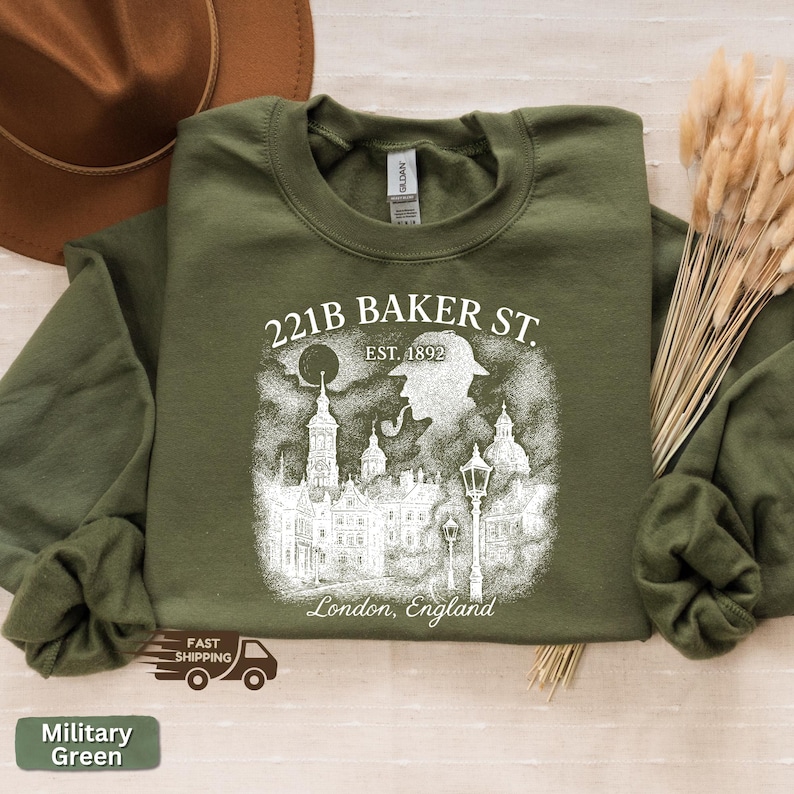 May include: A military green sweatshirt with a white graphic. The graphic includes the text "221B BAKER ST. EST. 1892 London, England" and a silhouette of a person with a pipe and a city scene.