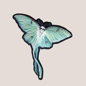 May include: A green and white embroidered patch of a luna moth with its wings spread out.