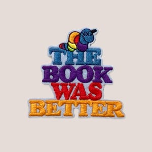 Op de afbeelding: Een geborduurde patch met een kleurrijke worm en de tekst "The Book Was Better".