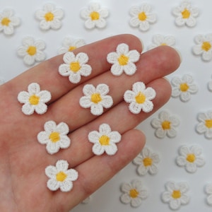 Peut inclure: Petites écussons de fleurs de marguerite blanches avec des centres jaunes. Ces appliqués brodés sont idéaux pour ajouter une touche florale aux vêtements ou aux projets d'artisanat. Les écussons présentent un design détaillé.