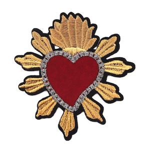 Op de afbeelding: Geborduurde patch met een rood hart met een zilveren rand, omringd door gouden stralen en een zwarte omtrek. De patch heeft een gedetailleerd, gestructureerd ontwerp, geschikt voor het verfraaien van kleding of accessoires.