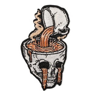 Pode incluir: Patch bordado com um desenho de caveira com uma chávena de café a ser derramada na cabeça da caveira. A caveira é branca com órbitas oculares pretas e lágrimas laranja. O café é laranja e o patch tem uma borda preta.