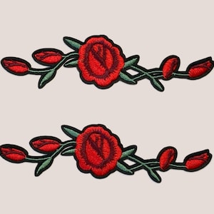 Könnte beinhalten: Zwei gestickte rote Rosen-Patches mit grünen Blättern und Stielen. Die Rosen blühen und die Stiele haben Knospen.