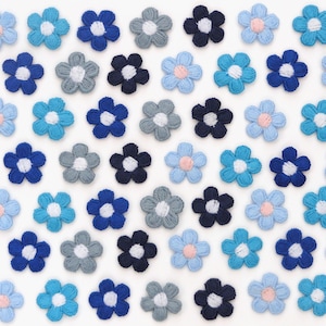 May include: An array of small, embroidered flower appliques in various shades of blue, gray, and white. The flowers have a detailed, textured appearance, with some featuring a pink center. The appliques are arranged closely together, creating a pattern.