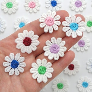 May include: White daisy flower patches with embroidered centers in various colors, including pink, blue, purple, green, and red. These small, decorative floral appliques are ideal for crafting and embellishing clothing or accessories.