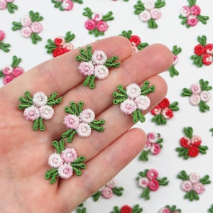 May include: Embroidered floral appliques in shades of pink and red with green stems and leaves. These small, detailed flower patches are ideal for embellishing clothing, accessories, or craft projects. The appliques are scattered on a white surface.