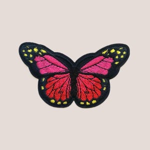 Pode incluir: Um remendo de borboleta bordado em rosa e amarelo com contornos pretos.