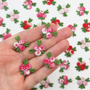 Könnte beinhalten: Gestickte Blumenapplikationen in verschiedenen Rosa-, Rot- und Weißtönen mit grünen Blättern. Diese kleinen, detaillierten Blumenaufnäher eignen sich perfekt zum Verzieren von Kleidung oder Bastelprojekten.