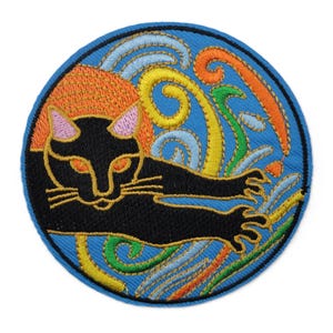 May include: Circular embroidered patch with a black cat design, set on a blue background with swirling patterns in orange, yellow, and green. The cat has orange eyes and pink ears. The patch is bordered with blue stitching, and the cat is in a relaxed pose.