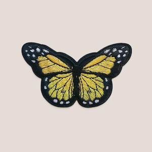 Pode incluir: Um remendo bordado de borboleta amarela com contornos pretos e pontos brancos. O remendo é perfeito para adicionar um toque de fantasia a roupas, bolsas ou outros acessórios.