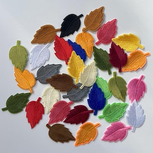 May include: A collection of 25 colorful felt leaf patches in various colors, including red, green, blue, yellow, brown, white, and pink. The leaves are all the same size and shape, and they are arranged in a random pattern.