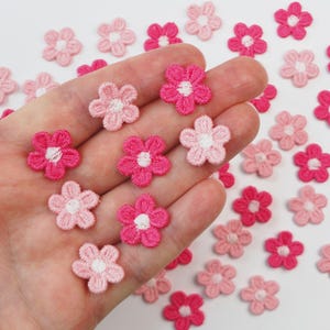 May include: A selection of small, embroidered flower appliques in shades of pink and fuchsia. The flowers have a six-petal design with a white centre. These decorative floral embellishments are ideal for craft projects.