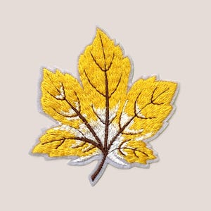 Peut inclure: Une feuille d'érable brodée jaune avec des nervures brunes et un centre blanc.