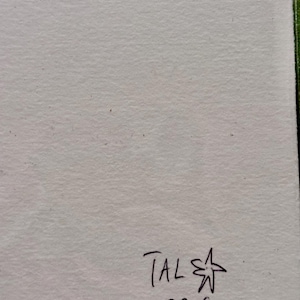 May include: A piece of off-white paper with the handwritten text "TAL" above "BERG" and a star symbol. The paper has a textured surface and a light colour.