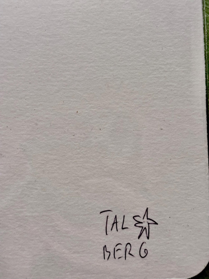 May include: A piece of off-white paper with the handwritten text "TAL" above "BERG" and a star symbol. The paper has a textured surface and a light colour.