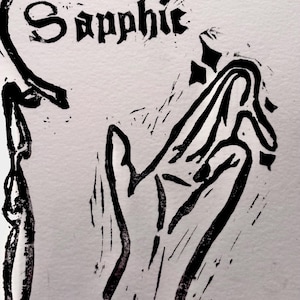 May include: A black and white linocut print with the word "Sapphic" in a gothic font. The print depicts a stylized hand and decorative border elements, all in bold black ink on a light background.