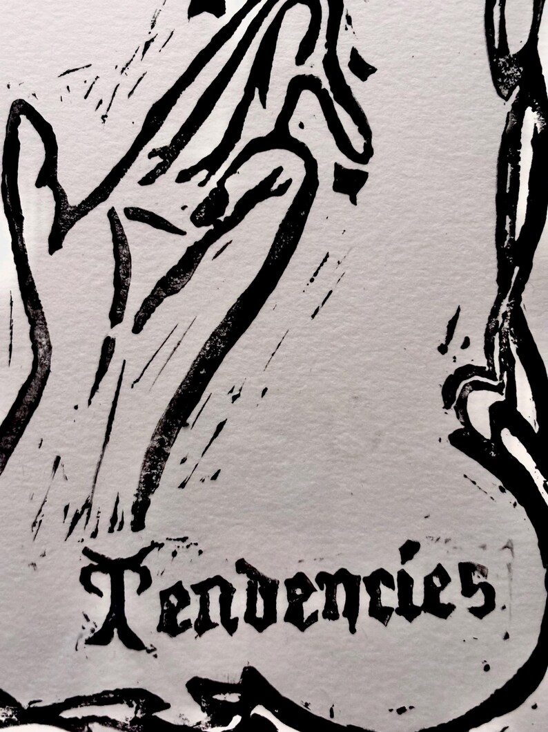 May include: A black and white linocut print with the word "Tendencies" in a gothic font. The artwork depicts stylized hands and abstract shapes, forming a striking and artistic design.