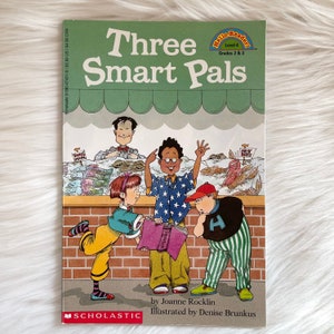 May include: A children's book cover with a green background and the title "Three Smart Pals". The cover features three children, one holding a book, another holding a fish, and the third looking at a book. The book is part of the "Hello Reader" series, level 4, for grades 2 and 3.