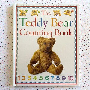 May include: A children's book titled "The Teddy Bear Counting Book" with a brown teddy bear sitting on a white background. The book cover features colorful numbers from 1 to 10.