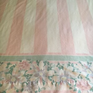 May include: A flat sheet with a pink and white striped pattern. The bottom edge features a floral design with pink, white, and purple flowers on a green and pink striped border. The sheet is made of a soft, possibly cotton, material.