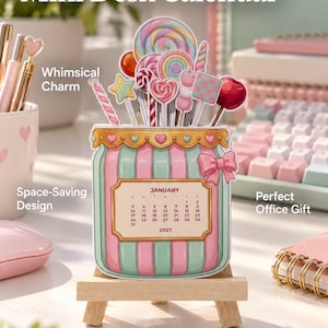 May include: A 2027 mini desk calendar shaped like a jar with pink and teal stripes, featuring a January 2027 calendar page. The jar is topped with colorful candy illustrations including lollipops and marshmallows, and it rests on a small wooden easel stand.