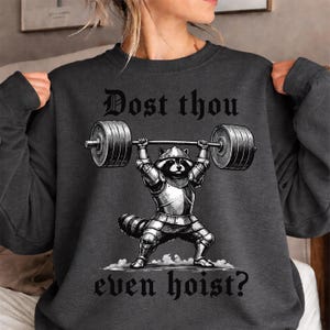Może przedstawiać: Ciemnoszara bluza z czarno-białą ilustracją szopa w zbroi podnoszącego sztangę. Tekst "Dost thou even hoist?" jest wydrukowany nad i pod ilustracją.