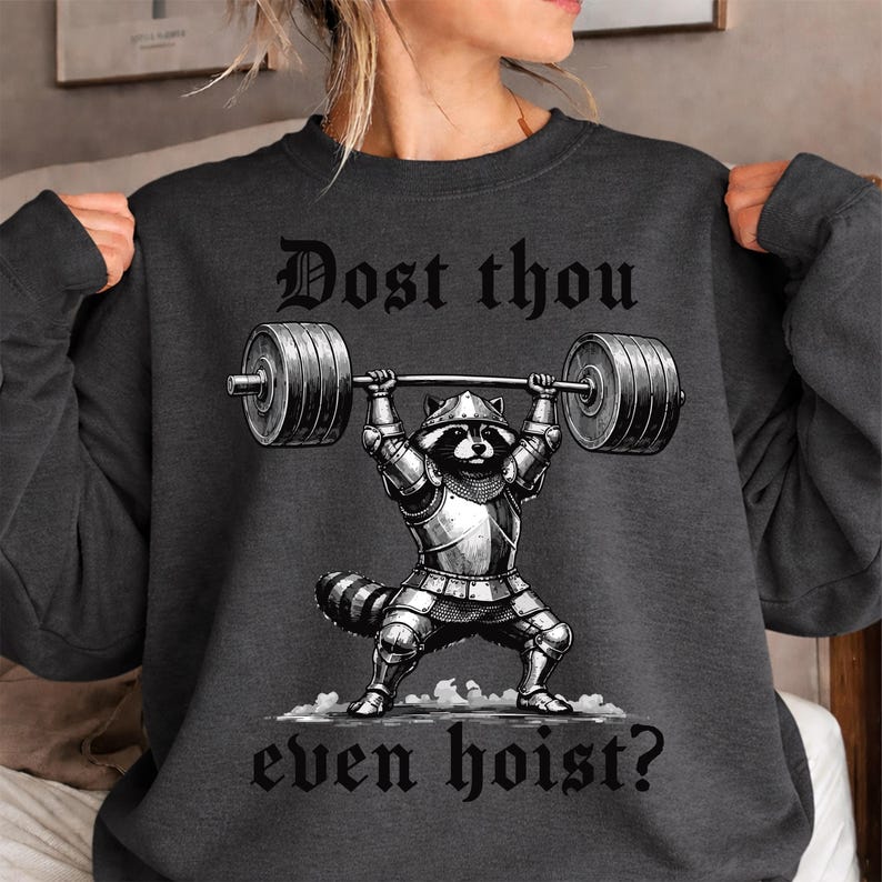 Może przedstawiać: Ciemnoszara bluza z czarno-białą ilustracją szopa w zbroi podnoszącego sztangę. Tekst "Dost thou even hoist?" jest wydrukowany nad i pod ilustracją.