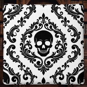 May include: A square throw pillow featuring a white fabric base with a repeating black damask pattern. The central design showcases a black human skull enclosed within an ornate, symmetrical scrollwork frame accented with fleur-de-lis motifs.