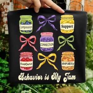Może przedstawiać: Czarny materiał z kolorową grafiką słoików z dżemem i kokardkami. Każdy słoik zawiera owoce i słowo: Compassion, Support, Connection, Acceptance i Adaptability. Tekst "Behavior is My Jam" znajduje się na dole.