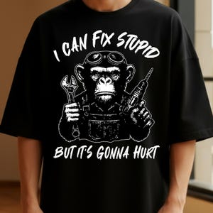 May include: Black t-shirt with a white graphic of a chimpanzee wearing goggles and overalls, holding a wrench and a drill. The text "I CAN FIX STUPID" is above the chimpanzee, and "BUT IT'S GONNA HURT" is below.