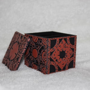 May include: A black and red wooden box with a intricate design. The box is open and the lid is laying next to it.