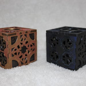 May include: Two decorative wooden boxes with intricate geometric designs. One box is painted a dark brown color and the other is painted black.
