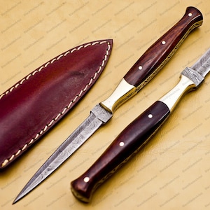 May include: A pair of decorative daggers with wood handles and brass accents. The blades are made of Damascus steel and have a unique pattern. The daggers come with a leather sheath.