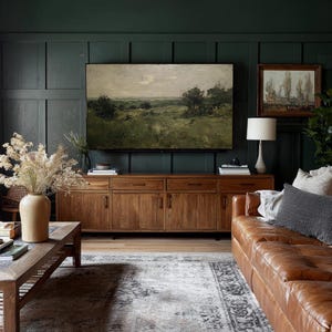 May include: A living room with a dark green paneled wall, featuring a large landscape painting above a wooden cabinet. A brown leather sofa and a patterned rug complete the space. A lamp and decorative vase are also visible.