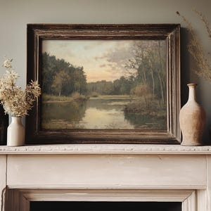 May include: A vintage framed landscape painting of a lake surrounded by trees, hanging above a white mantelpiece with two vases and a single vase with dried flowers.