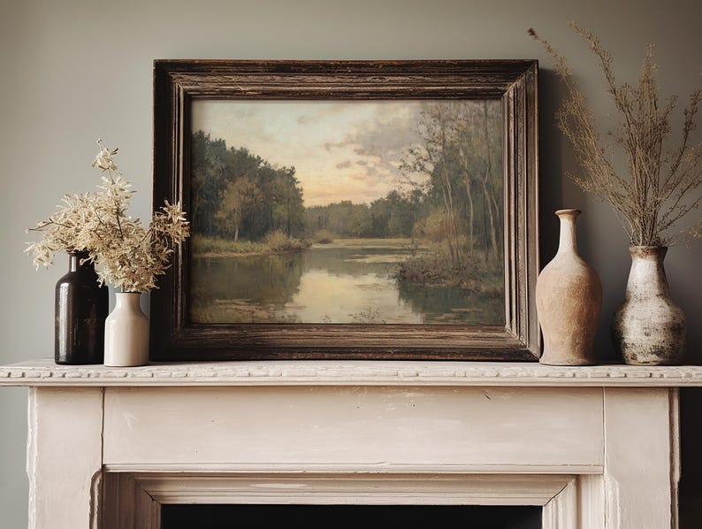 May include: A vintage framed landscape painting of a lake surrounded by trees, hanging above a white mantelpiece with two vases and a single vase with dried flowers.