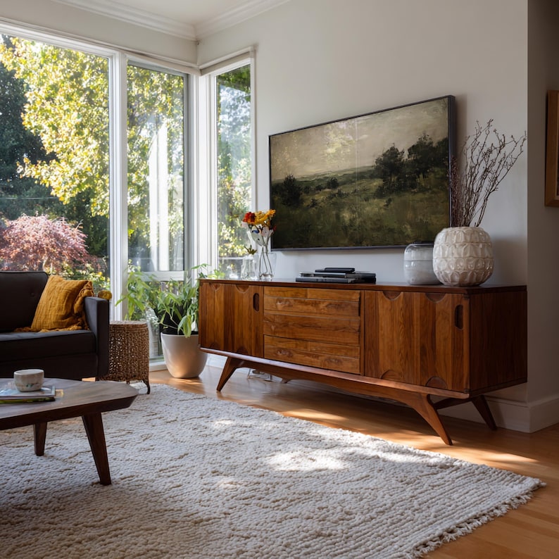 May include: A mid-century modern wooden sideboard featuring a long rectangular frame with two side cabinets and three central drawers, supported by four angled legs. The piece has a rich brown wood grain finish and recessed handle cutouts.