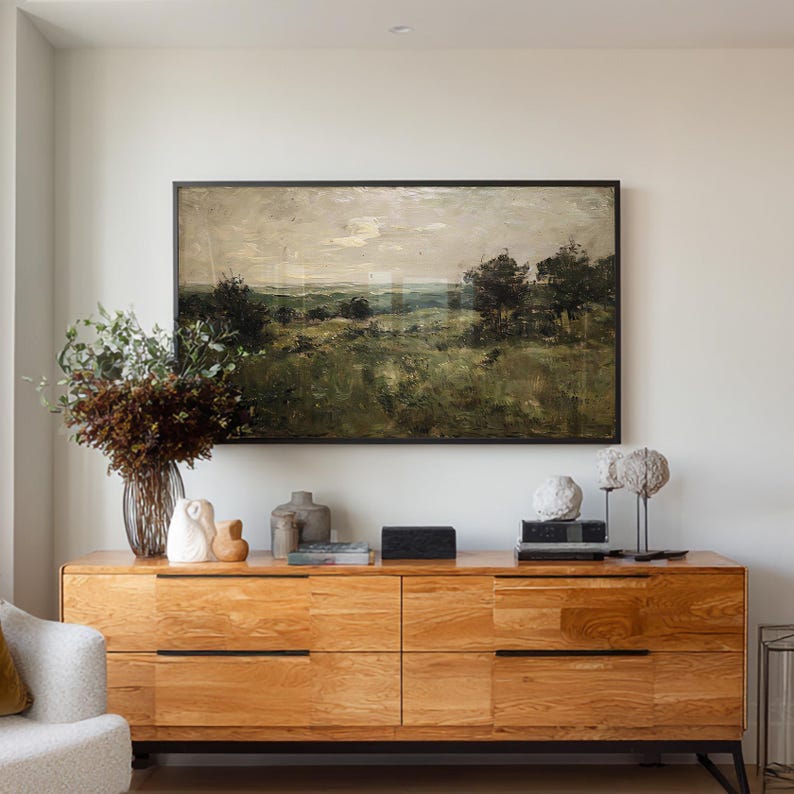 May include: A wooden dresser with six drawers, topped with decorative items and a framed landscape painting. The painting depicts a field with trees under a cloudy sky. A vase of flowers and various sculptures are on the dresser.
