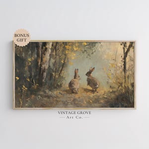 May include: A vintage painting of two brown rabbits in a forest setting. The rabbits are facing each other and are surrounded by trees and foliage. The painting is in a light brown frame and has a vintage feel.
