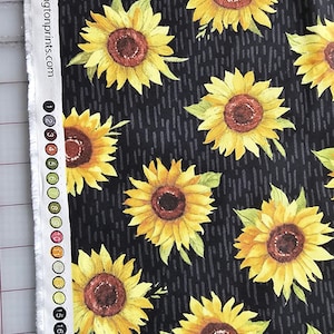 May include: Black fabric with a repeating pattern of yellow sunflowers with brown centers. The fabric has a white border with numbers 1-16 printed on it. The text "www.wilmingtonprints.com" is printed on the fabric.