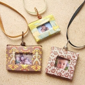 May include: Three necklaces with small picture frames as pendants. The frames are made of cardboard and decorated with patterned paper. Each frame has a different photo inside.